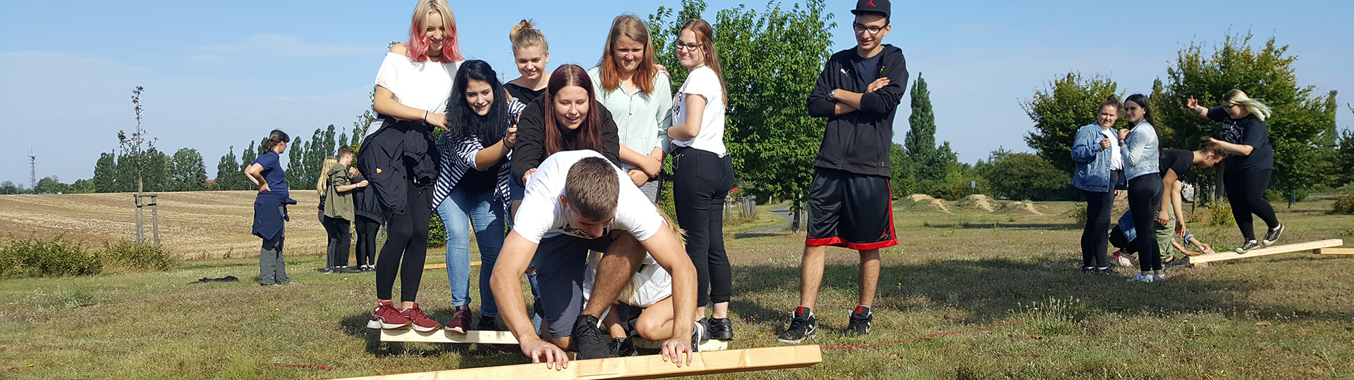 Eine Gruppe von Jugendlichen bei einer Team-Aufgabe mit Holzbalken